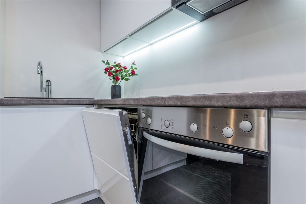 Built-in dishwasher with its door slightly open next to a wall oven in a white kitchen