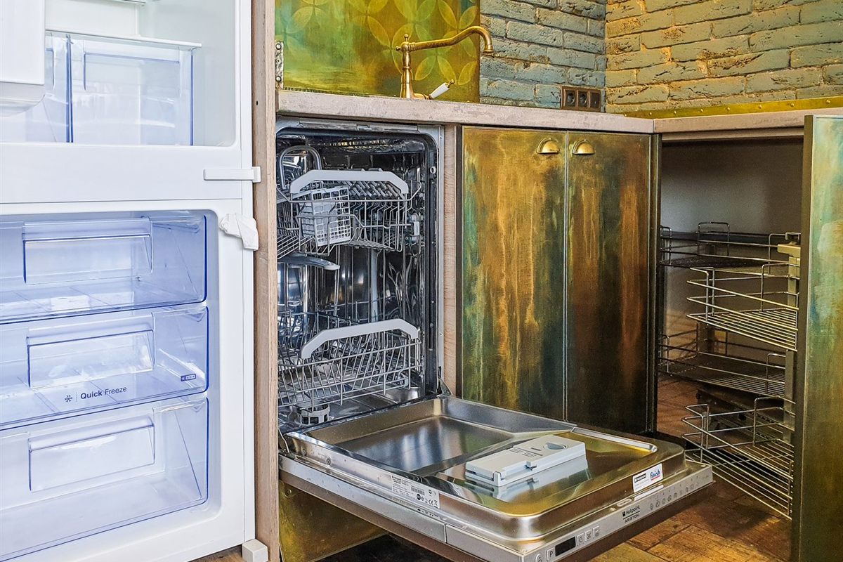 Open built-in dishwasher with empty racks below a kitchen sink and faucet