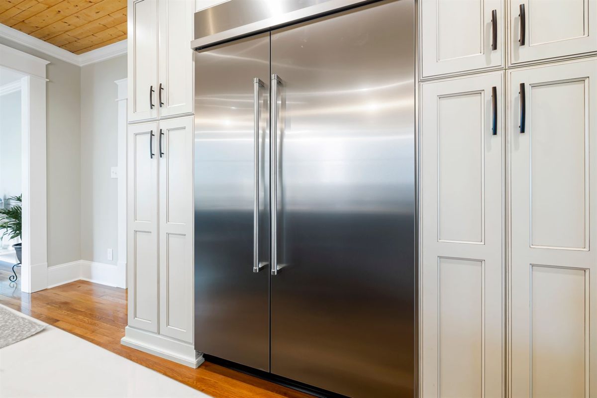 Stainless steel built-in refrigerator between white kitchen cabinets