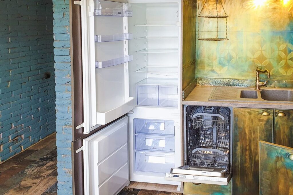 Open built-in refrigerator with empty shelves and freezer drawers in a home kitchen