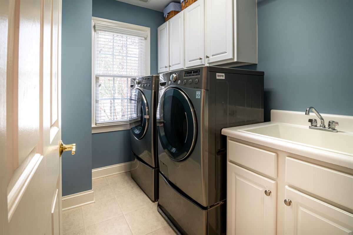 Front-load washer and dryer on pedestals next to a utility sink in a laundry room