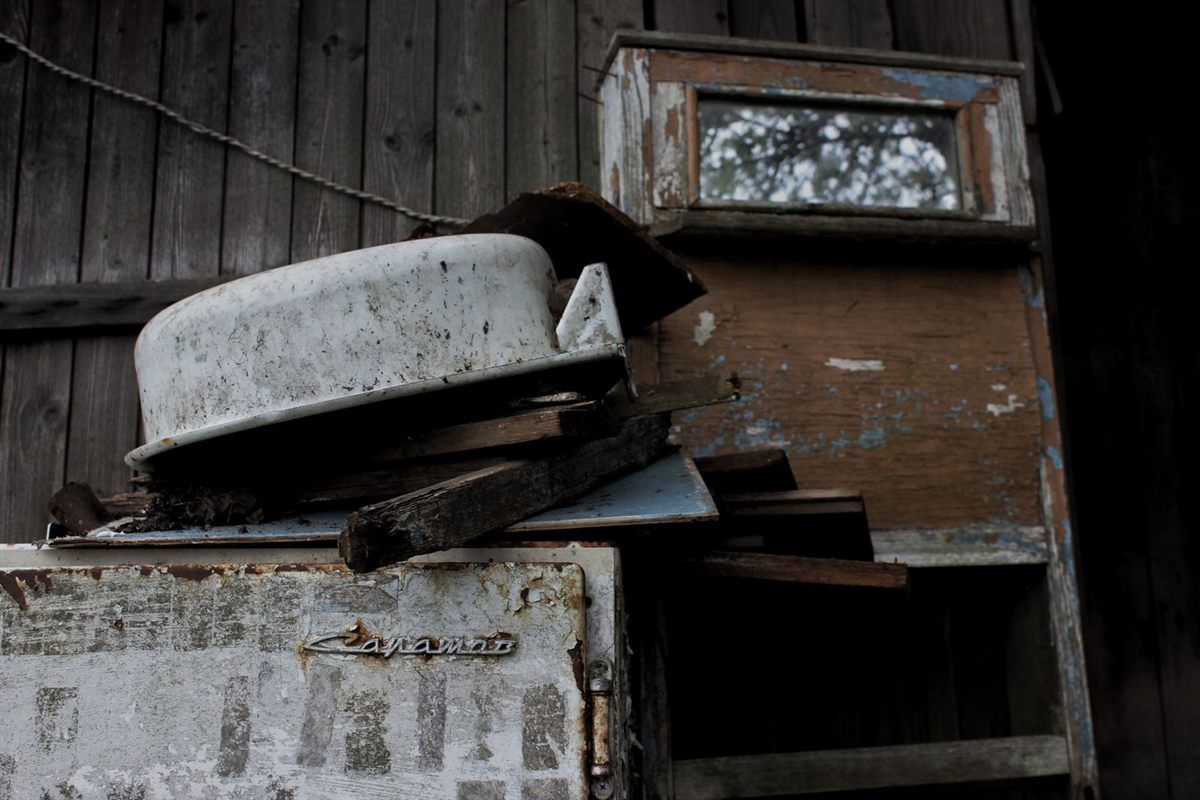 Old rusted refrigerator and other worn household items stored against a wooden wall