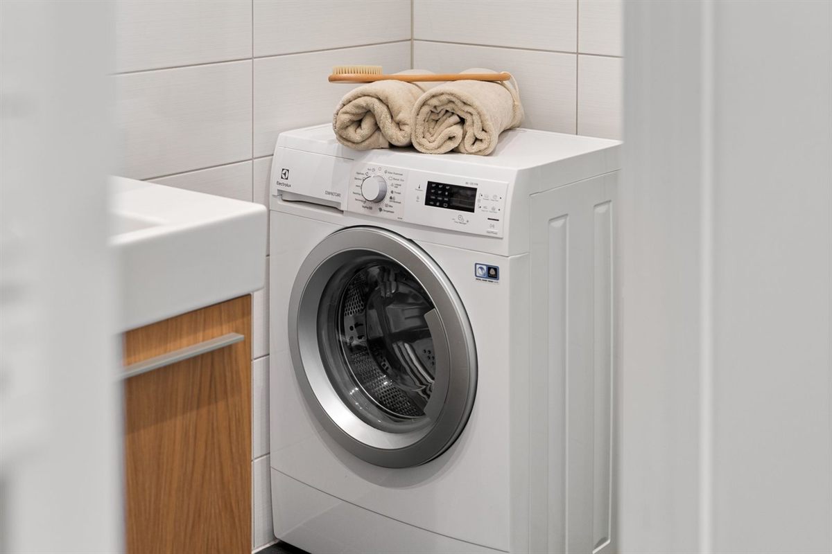 Compact front-load washing machine with towels on top in a tiled bathroom