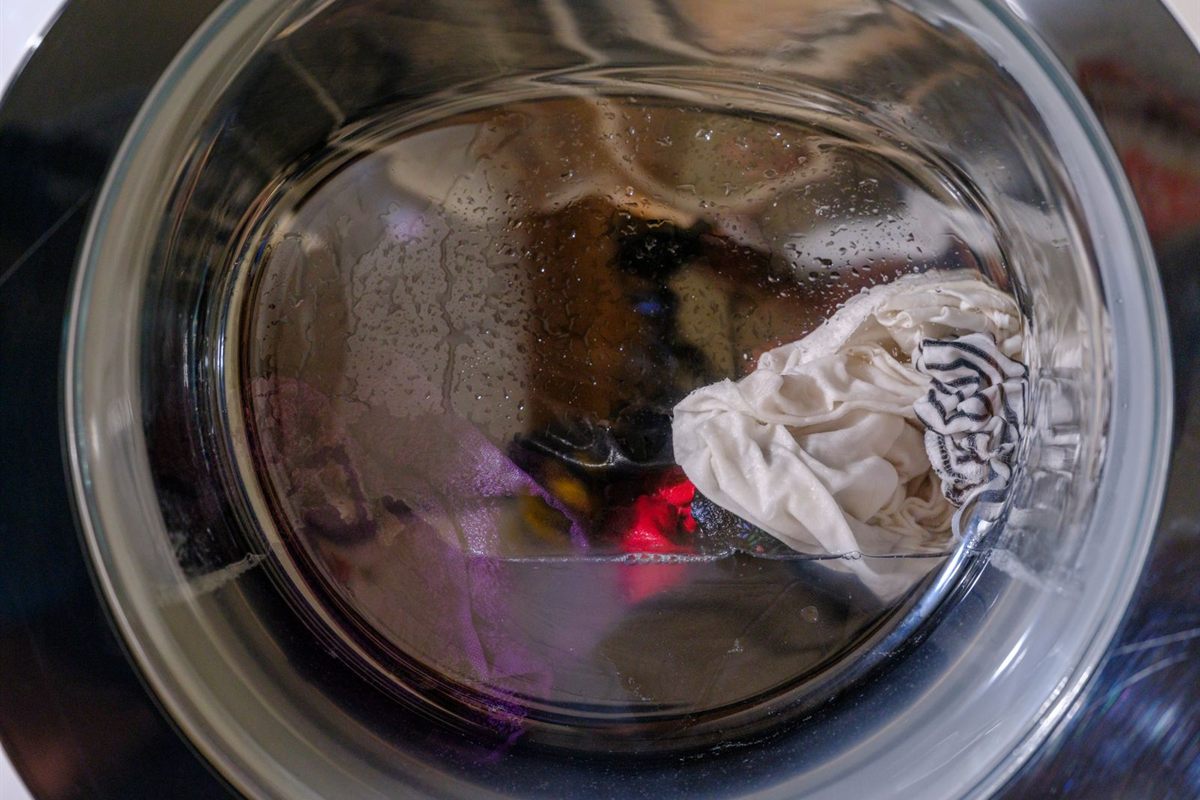 Wet laundry and standing water behind the glass door of a front-load washer
